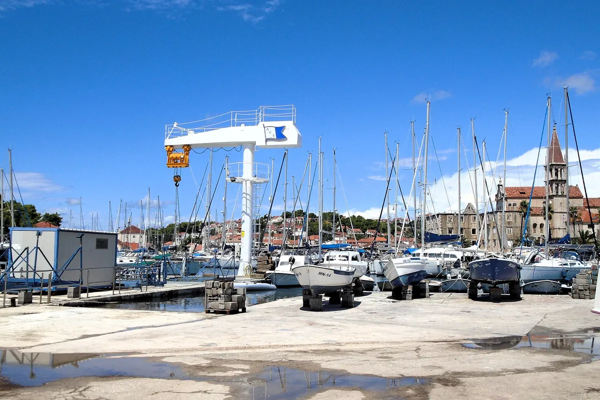 ACI Marina Milna at the head of Milna bay: yachts on the pontoons, boats on the hardstanding by the marina crane, and the bell tower of Milna church behind