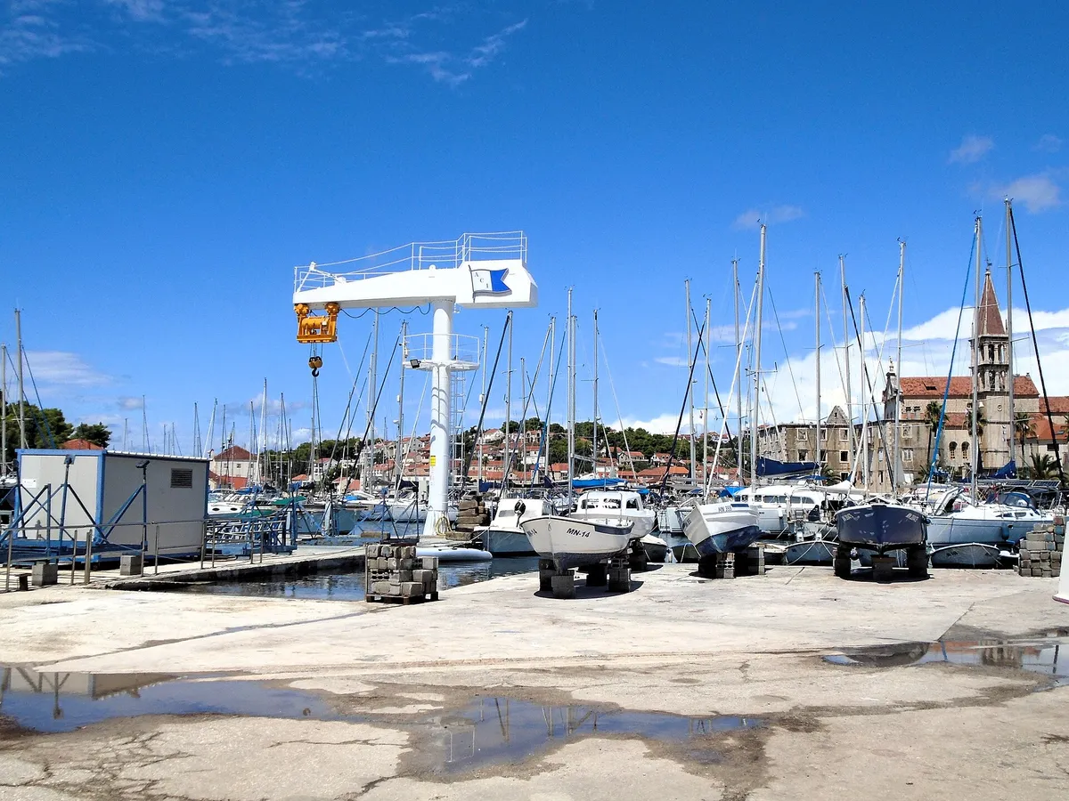 ACI Marina Milna at the head of Milna bay: yachts on the pontoons, boats on the hardstanding by the marina crane, and the bell tower of Milna church behind