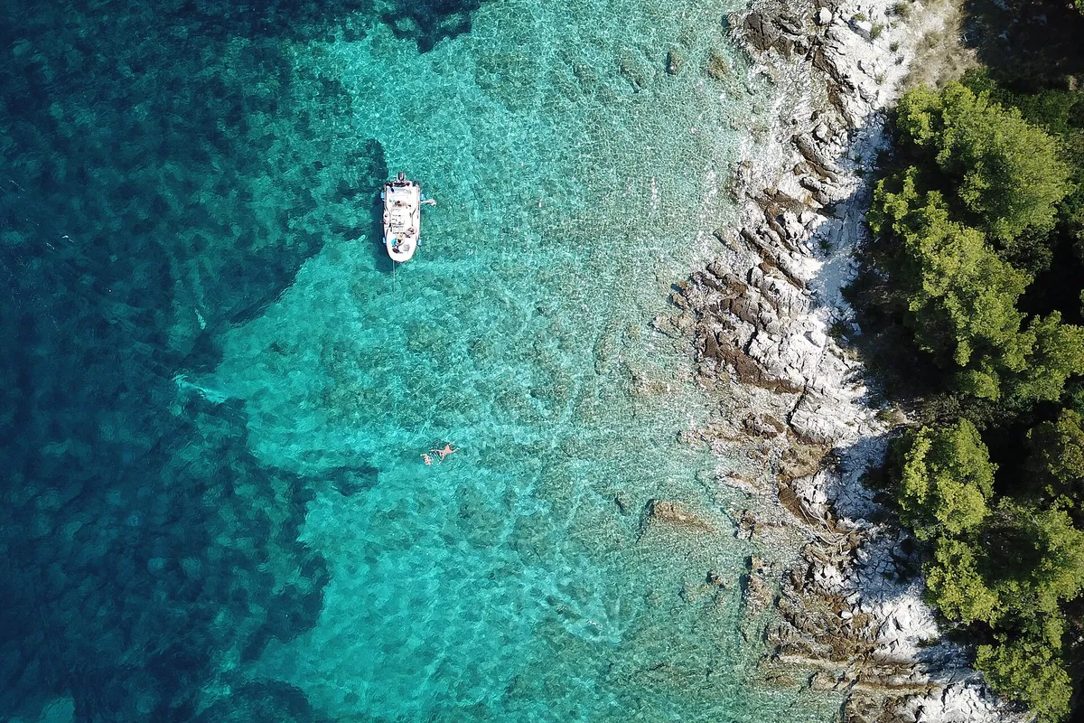 A small boat at anchor over sand and weed in clear water, straight-down drone view