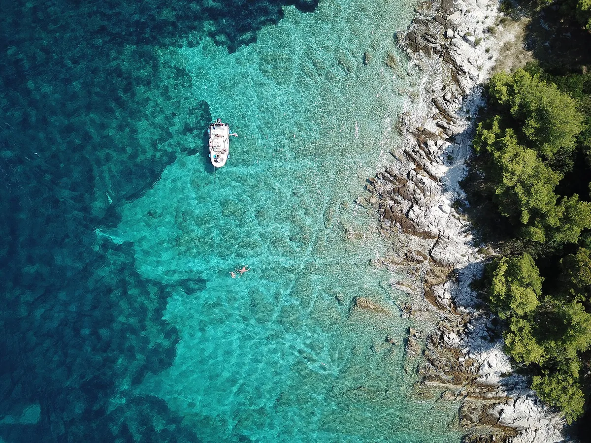 A small boat at anchor over sand and weed in clear water, straight-down drone view
