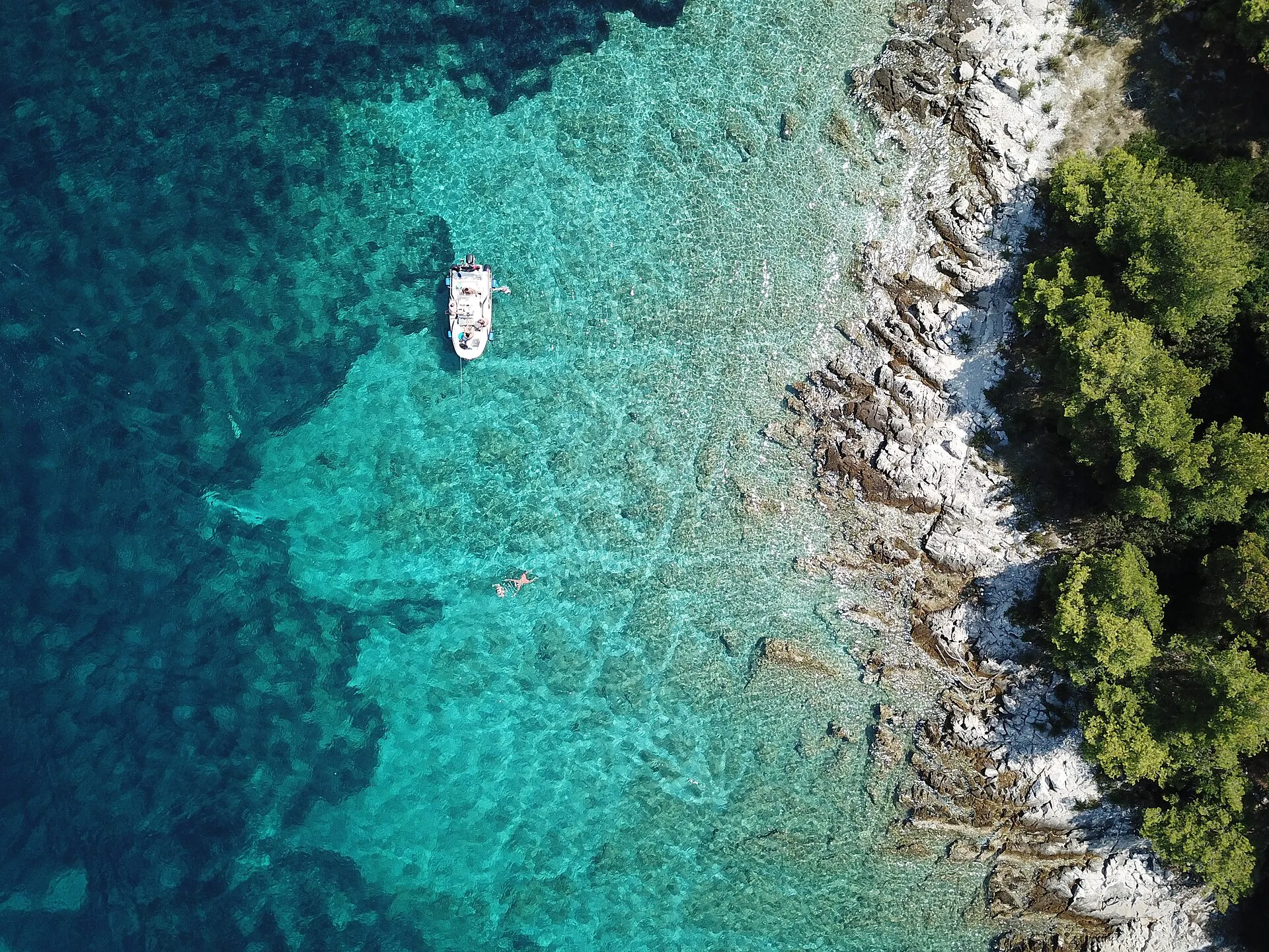 A small boat at anchor over sand and weed in clear water, straight-down drone view