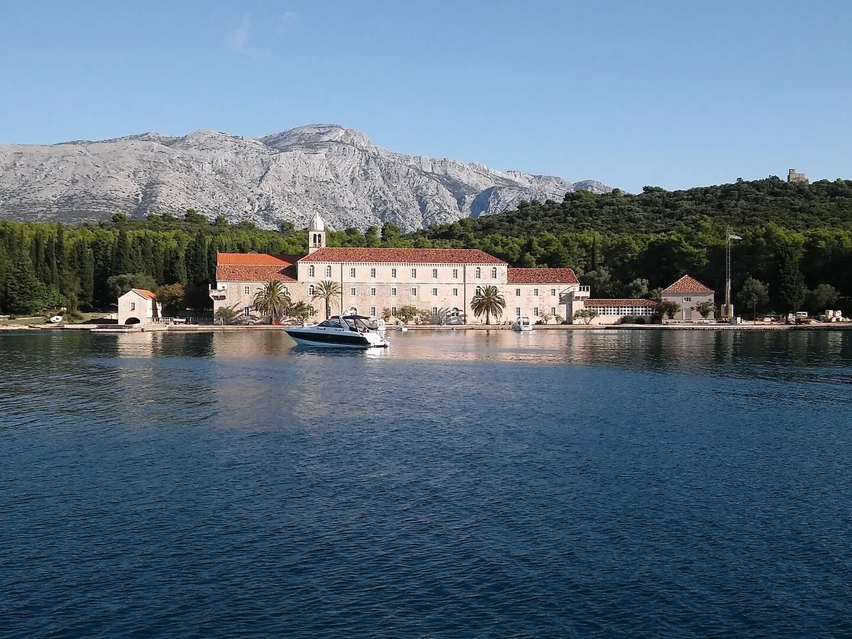 The Franciscan monastery on Badija seen from the water, its quay with a motorboat, pine woods behind and the mountains of Pelješac beyond