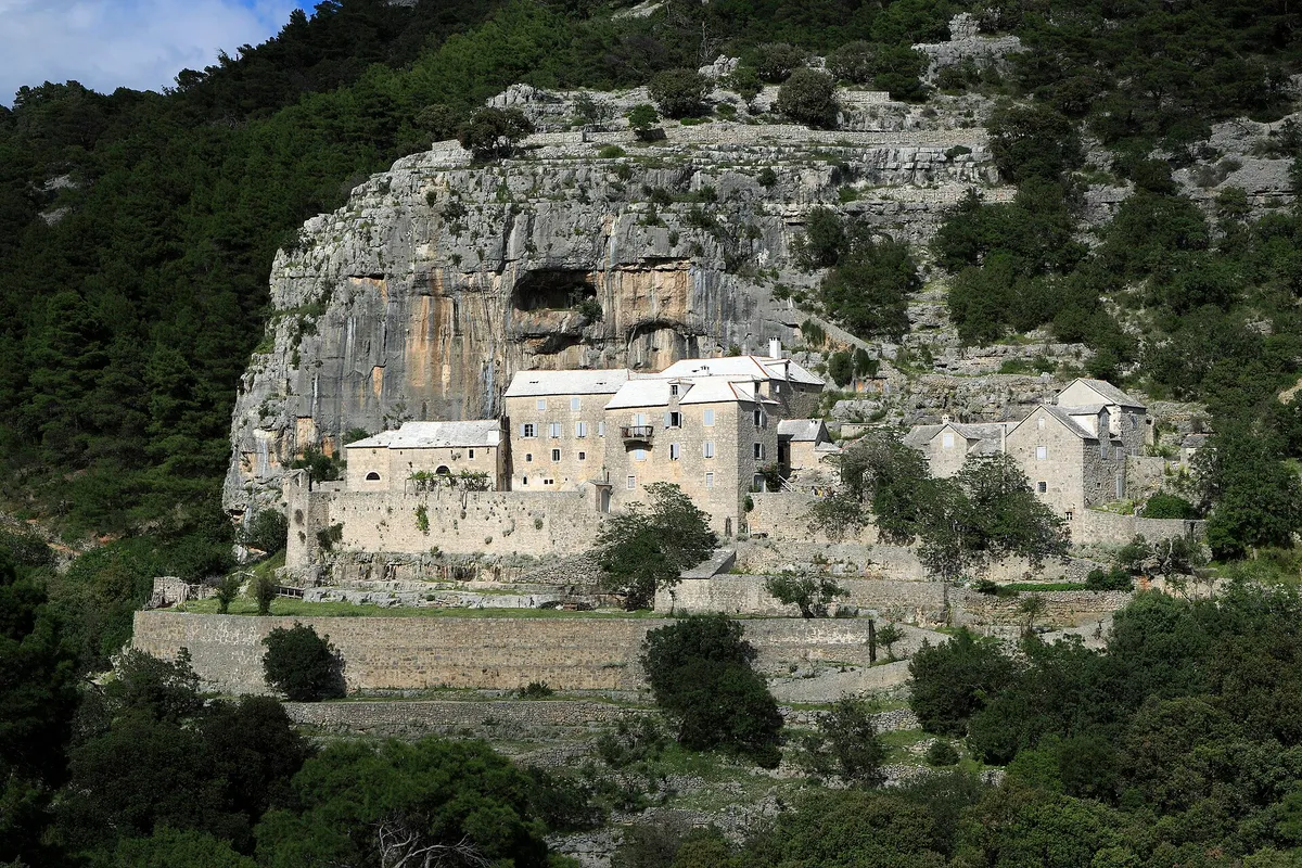 The Blaca hermitage, stone monastery buildings built against a cliff with a cave, in pine woods above the south coast of Brač.