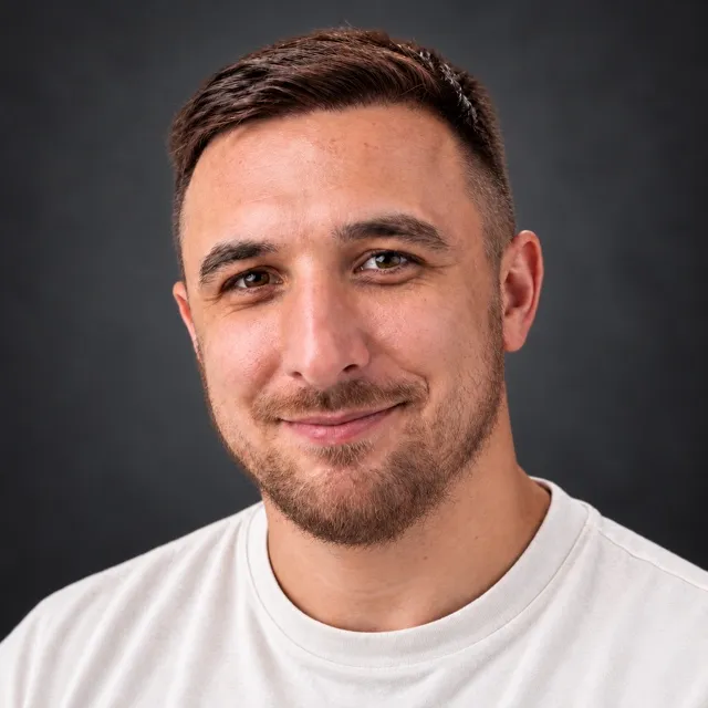 Domagoj Franc, head and shoulders, smiling, in a white T-shirt against a dark grey background