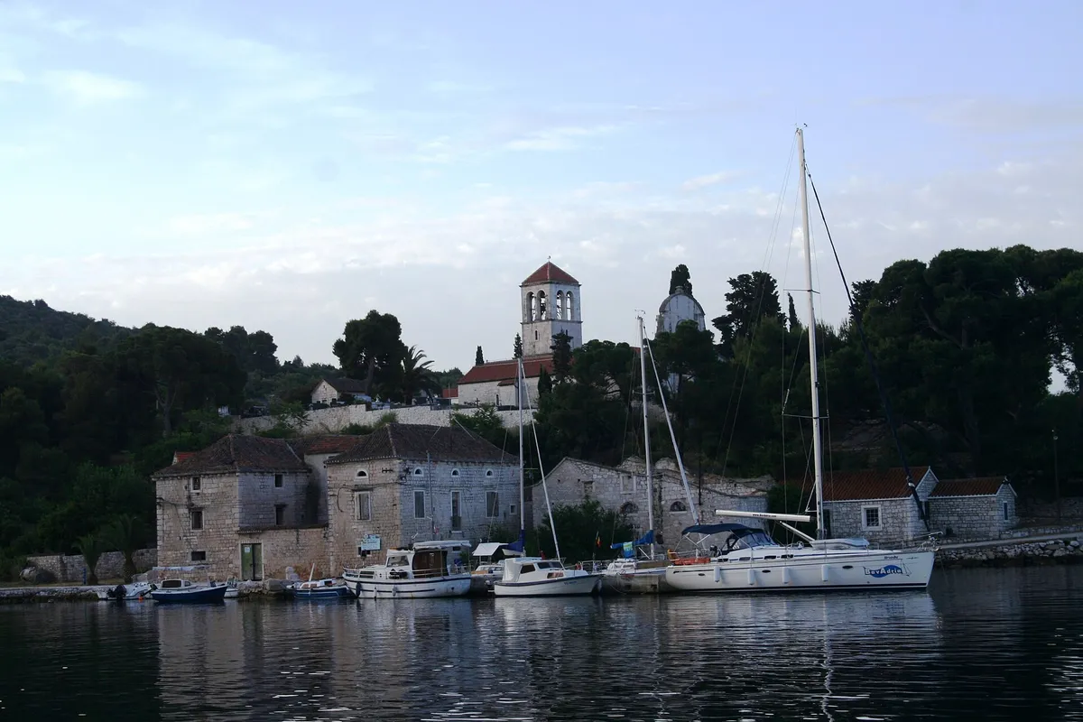 The harbour of Drvenik Veli seen from the water at dawn, yachts and local boats at the stone quay under the bell tower of St George's church