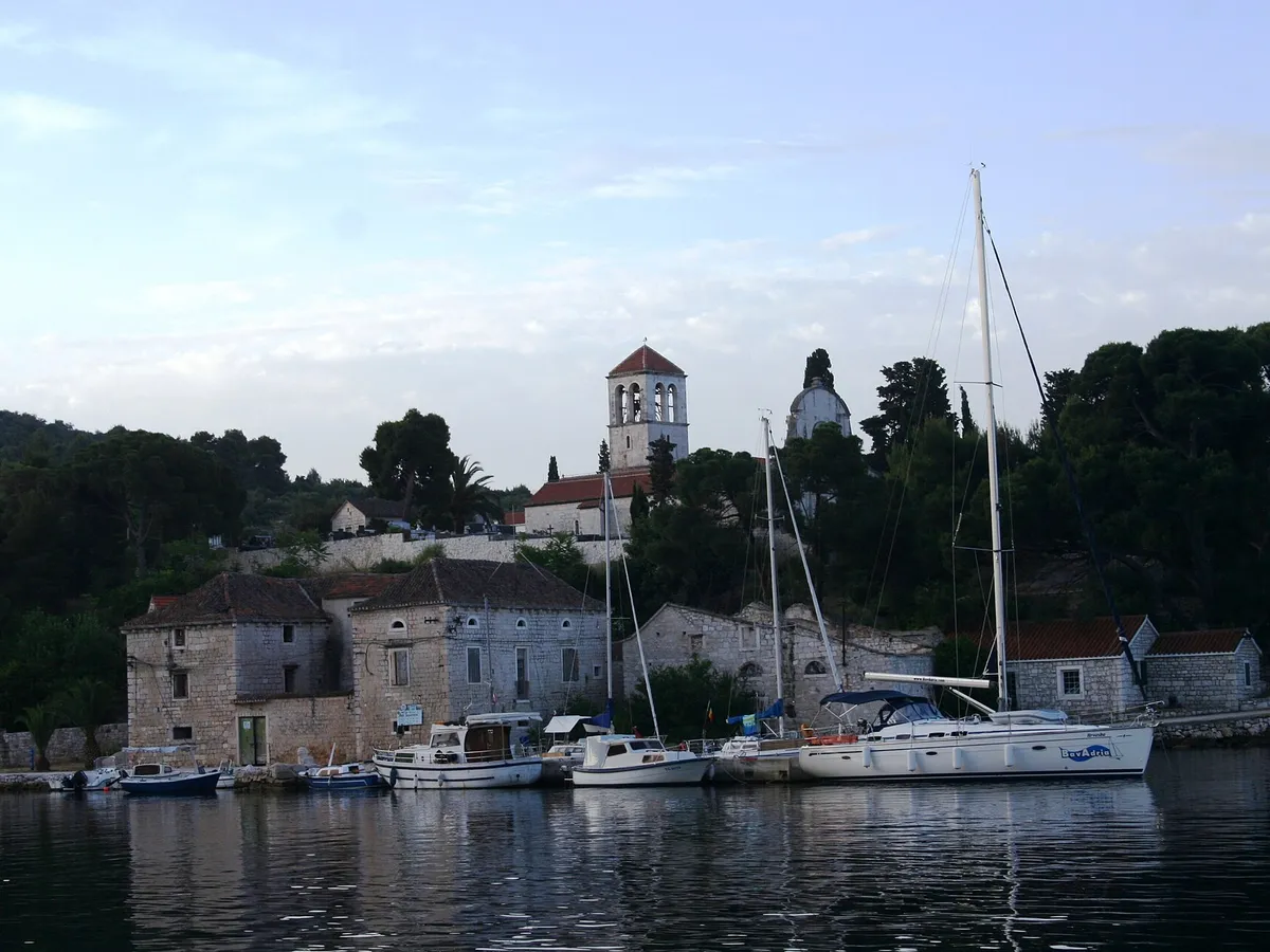 The harbour of Drvenik Veli seen from the water at dawn, yachts and local boats at the stone quay under the bell tower of St George's church