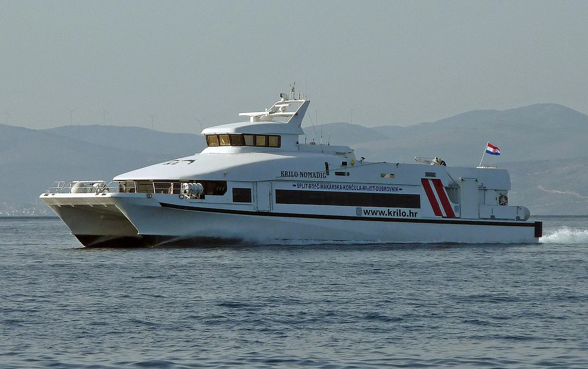 A fast passenger catamaran under way off Split at speed, its wake behind it and the mainland hills in the haze