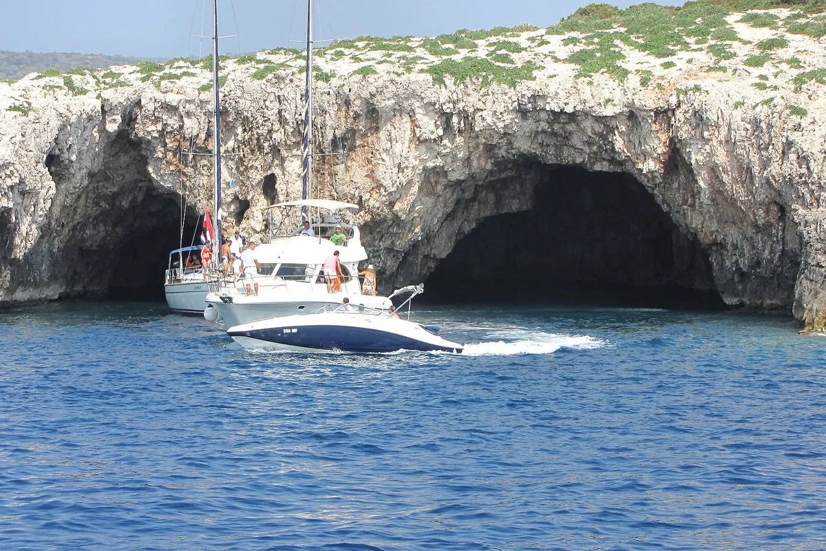 The two sea entrances of the Green Cave on Ravnik seen from the water, a sailing yacht and a motor cruiser at the mouth and a speedboat passing