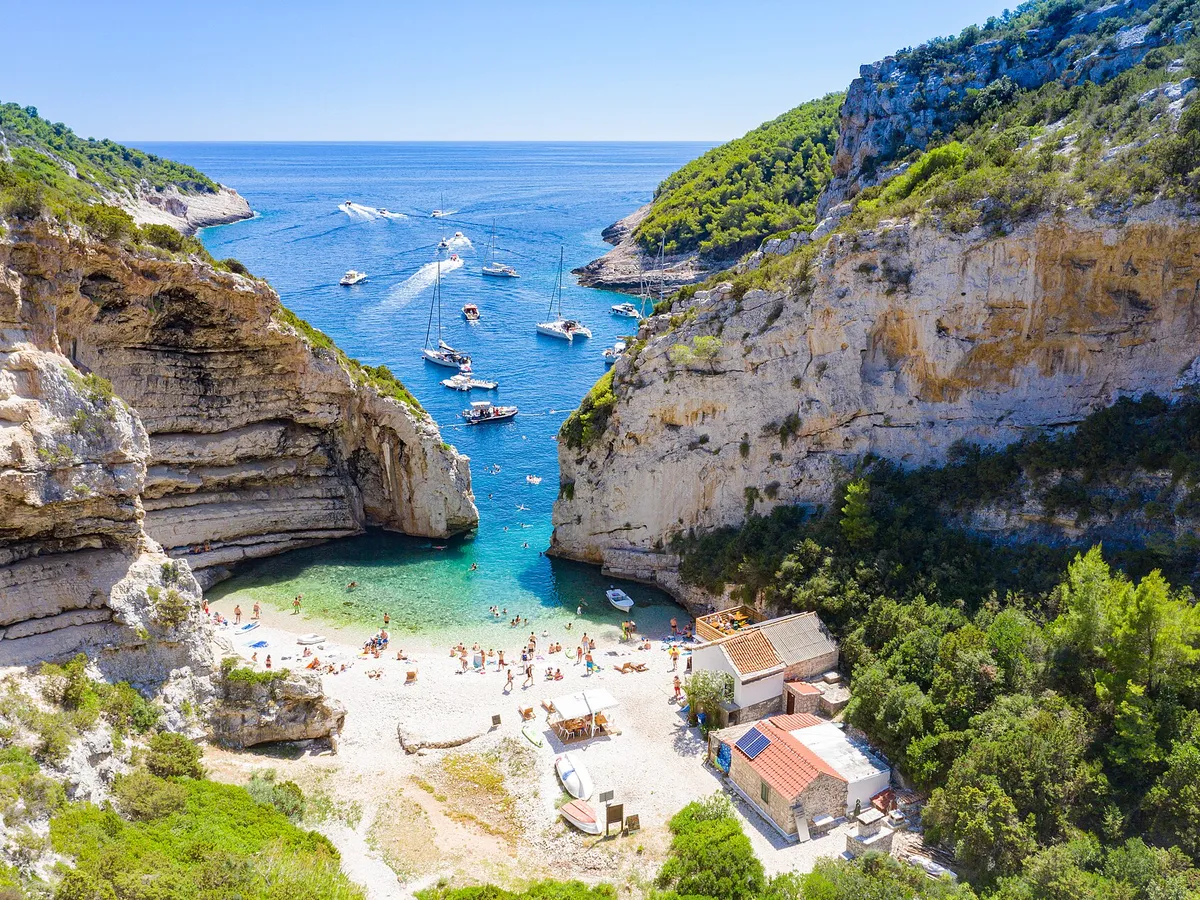 Sailing yachts anchored off the mouth of Stiniva cove, aerial with open sea and horizon