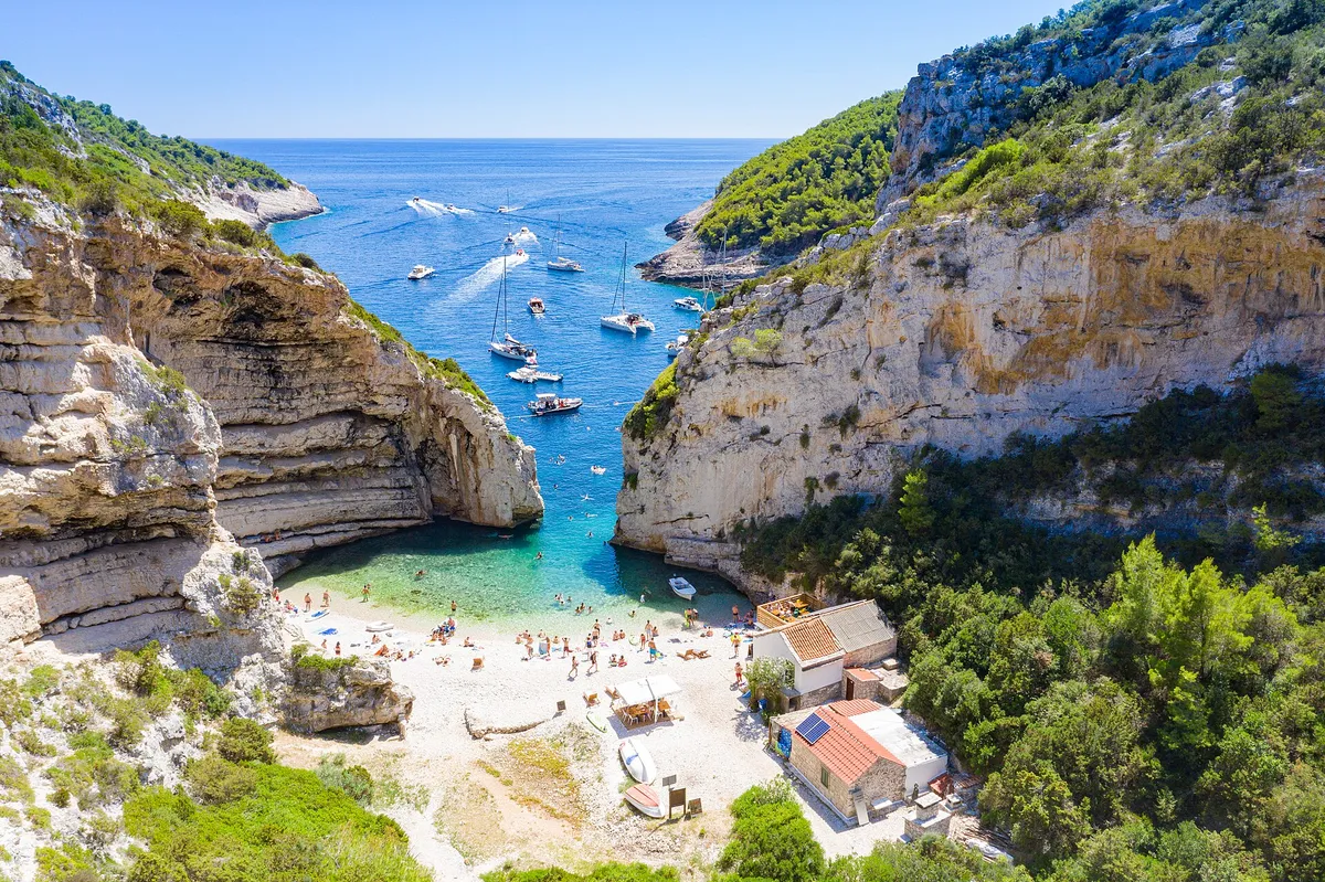 Sailing yachts anchored off the mouth of Stiniva cove, aerial with open sea and horizon