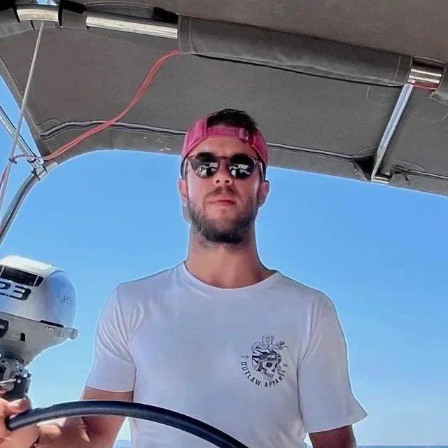 Ivor Benko at the helm of a sailing yacht, in a cap and sunglasses, with a blue sky behind