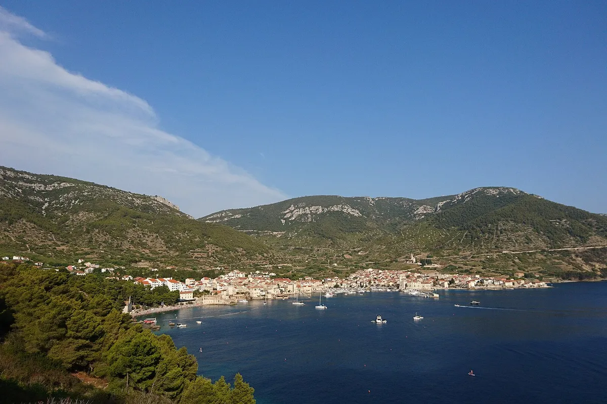 Komiža bay from the hillside, with boats at anchor in front of the town and the Hum hills behind.