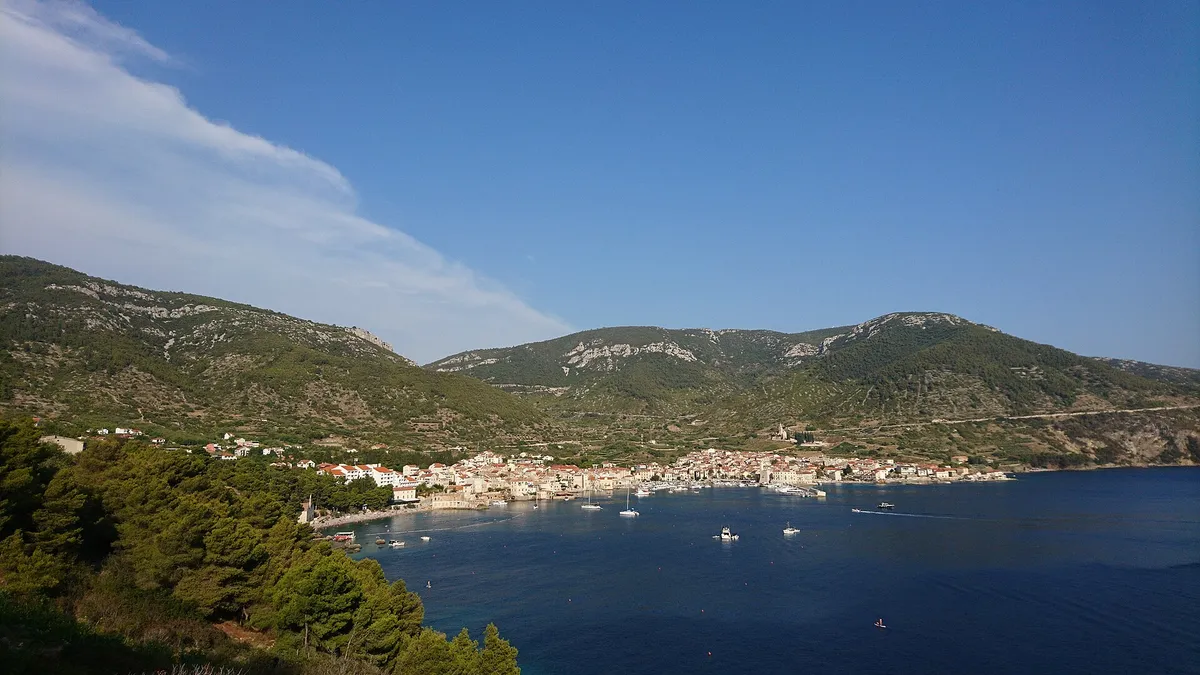 Komiža bay from the hillside, with boats at anchor in front of the town and the Hum hills behind.