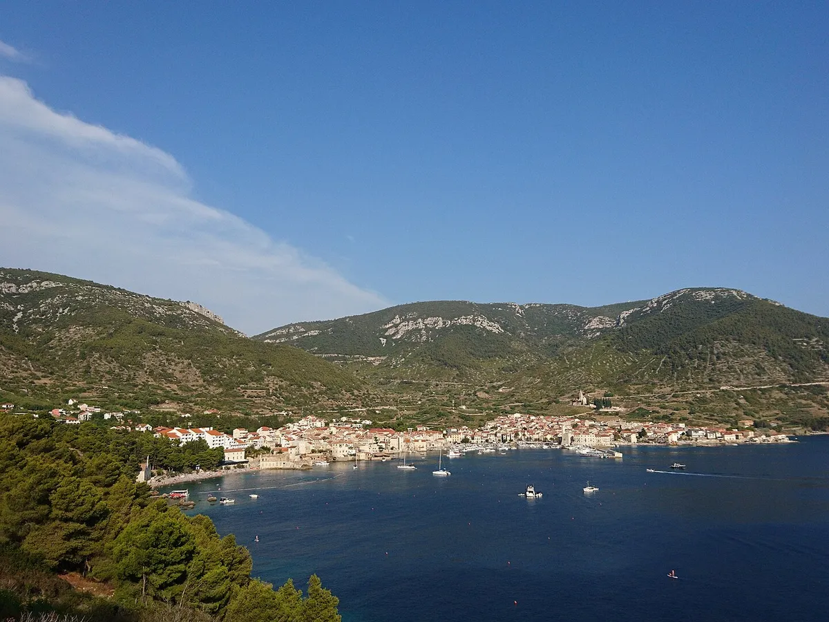 Komiža bay from the hillside, with boats at anchor in front of the town and the Hum hills behind.