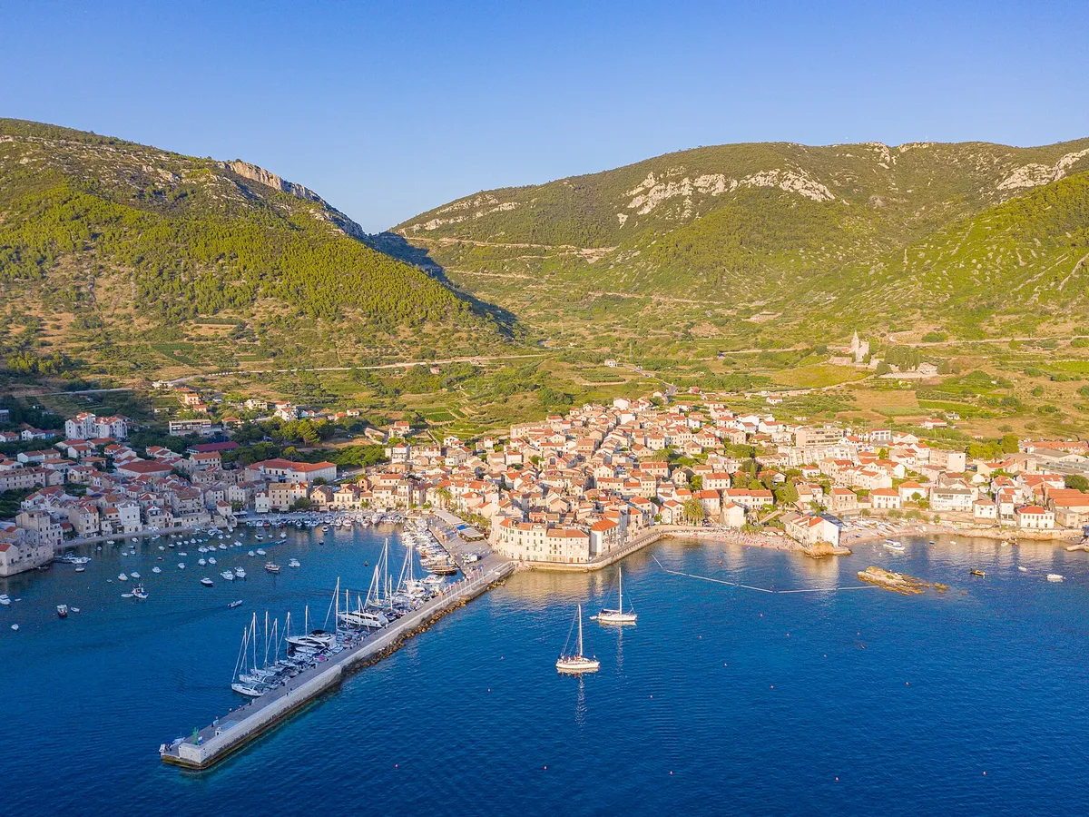 Aerial of Komiža harbour and town, yachts on the pier and at anchor, hills behind