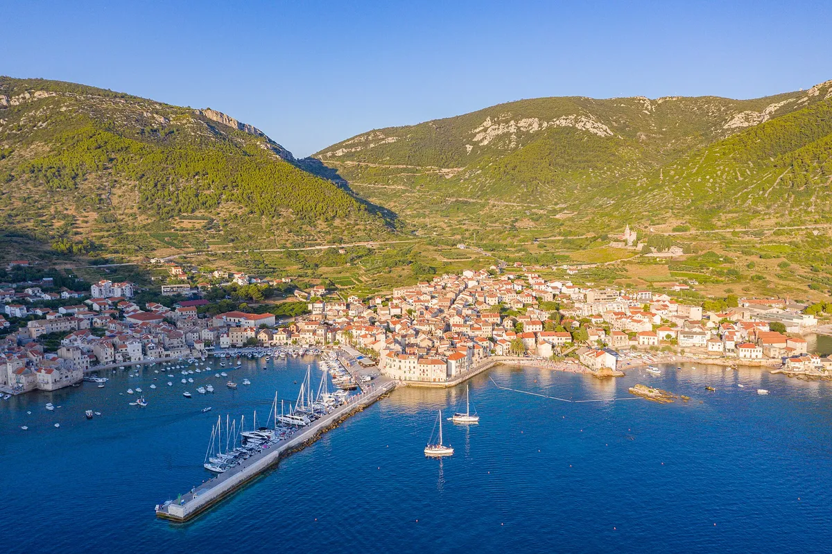 Aerial of Komiža harbour and town, yachts on the pier and at anchor, hills behind