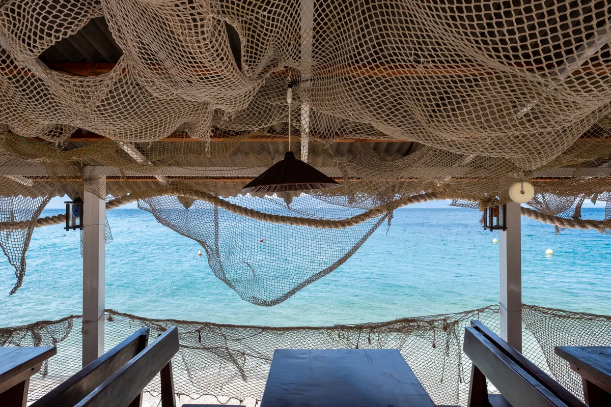 A fishing-themed Croatian restaurant terrace with tables under hanging nets and a view across bright blue sea