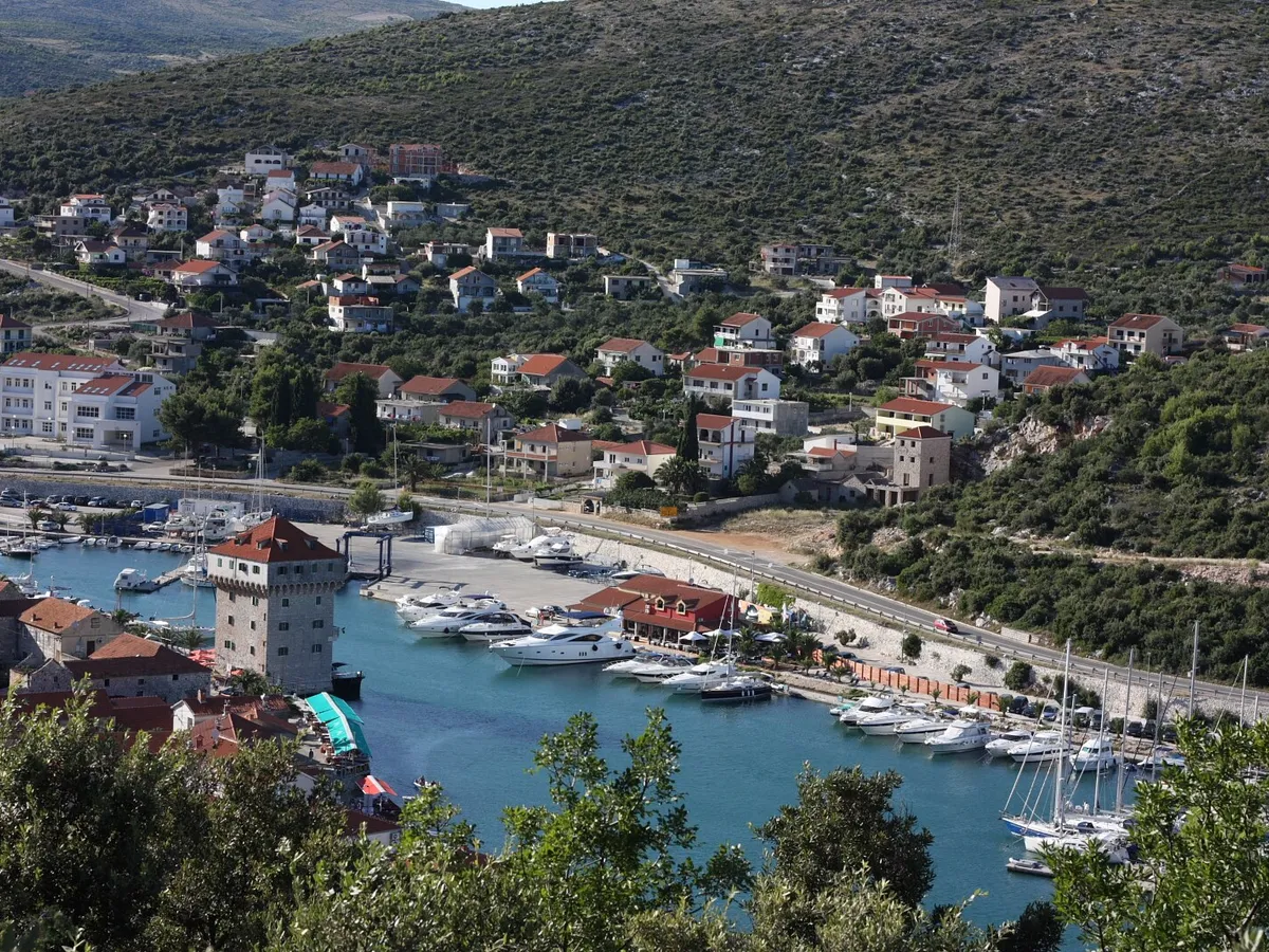 Marina Agana in Marina, west of Trogir, from the hill above: motor yachts and sailing yachts on the pontoons along the bay, the old tower on the waterfront and houses on the hillside