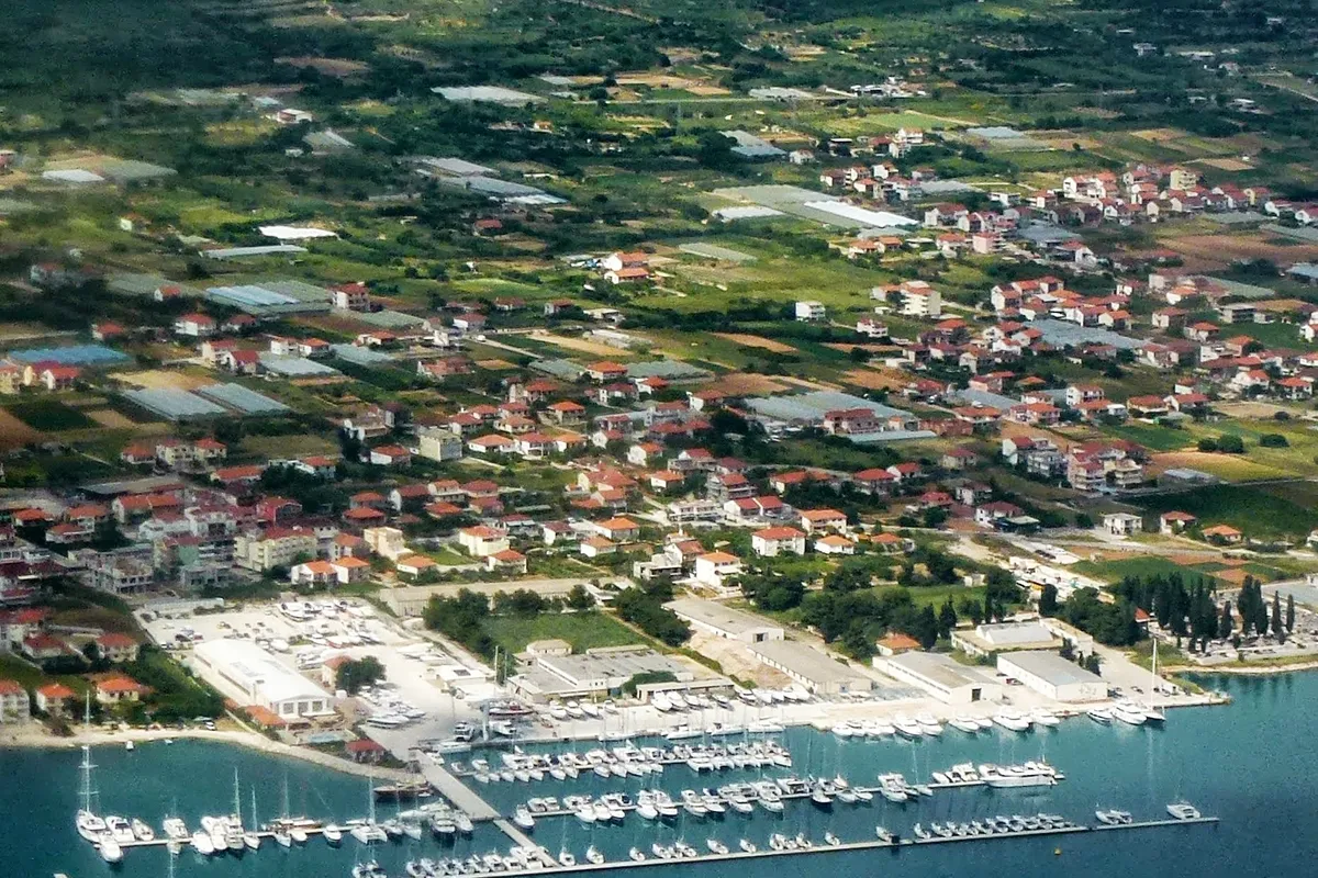 Marina Baotić at Seget Donji from the air: long pontoons full of yachts off the shore, the boatyard behind them and the village among fields