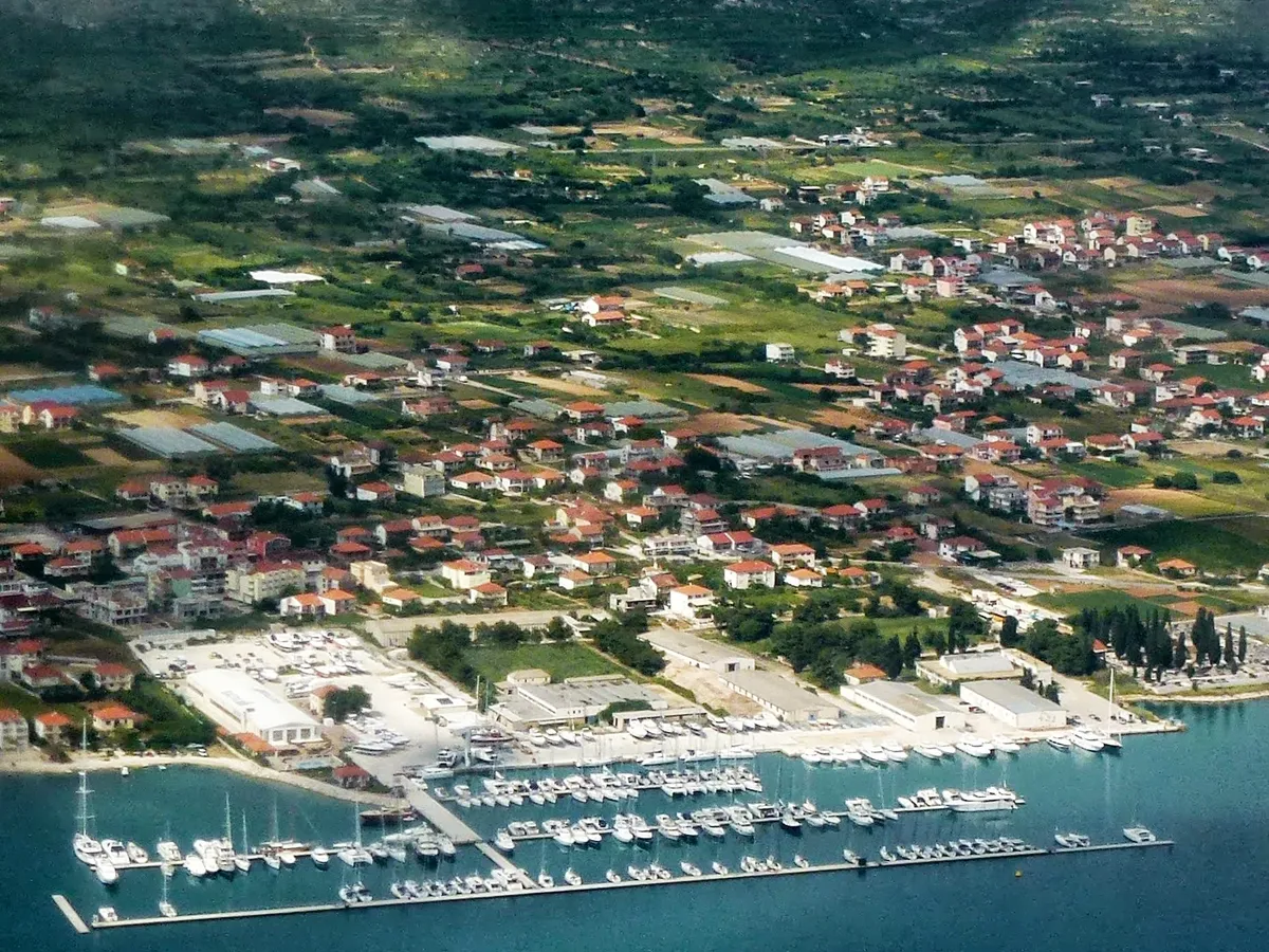 Marina Baotić at Seget Donji from the air: long pontoons full of yachts off the shore, the boatyard behind them and the village among fields