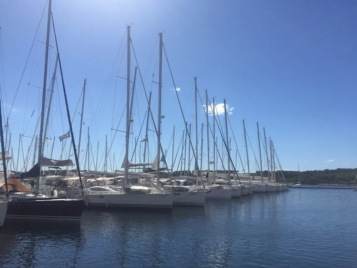 A long row of charter yachts moored stern-to on a pontoon at D-Marin Mandalina, Šibenik, under a clear sky