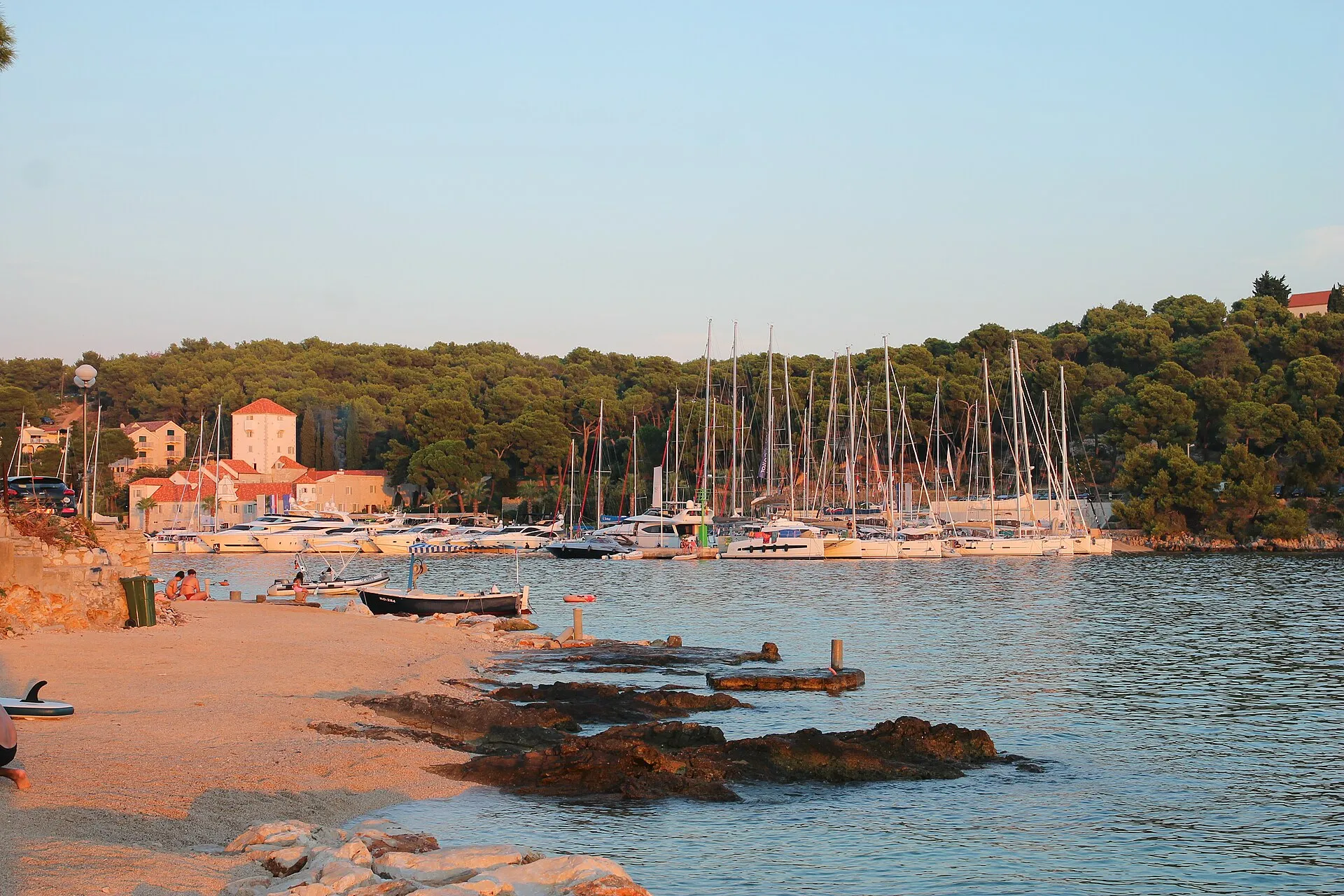 The marina in Maslinica bay on Šolta, with yachts on the pontoons, the old castle and a small beach in front.