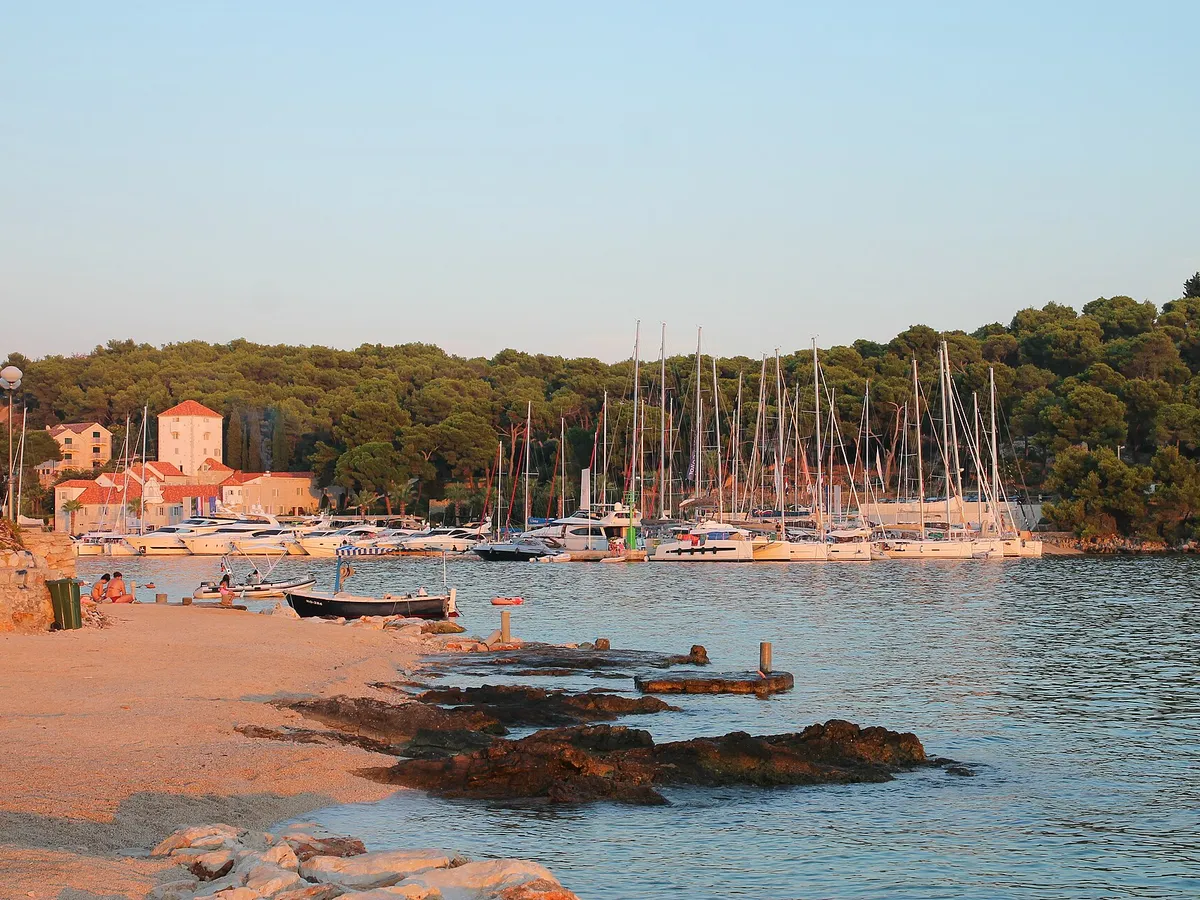 The marina in Maslinica bay on Šolta, with yachts on the pontoons, the old castle and a small beach in front.