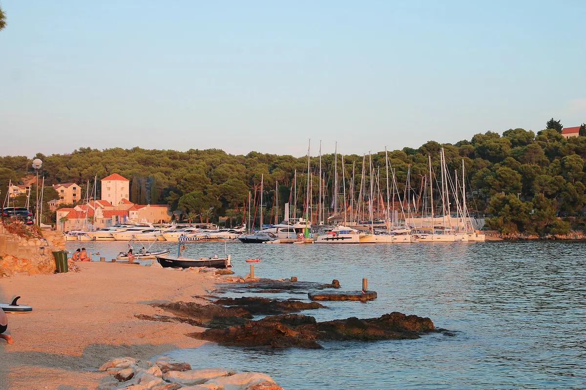 The marina in Maslinica bay on Šolta, with yachts on the pontoons, the old castle and a small beach in front.