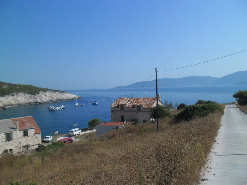 Mezuporat bay on Biševo from the road above, small boats and yachts moored in the blue bay below old stone houses, with Vis across the channel