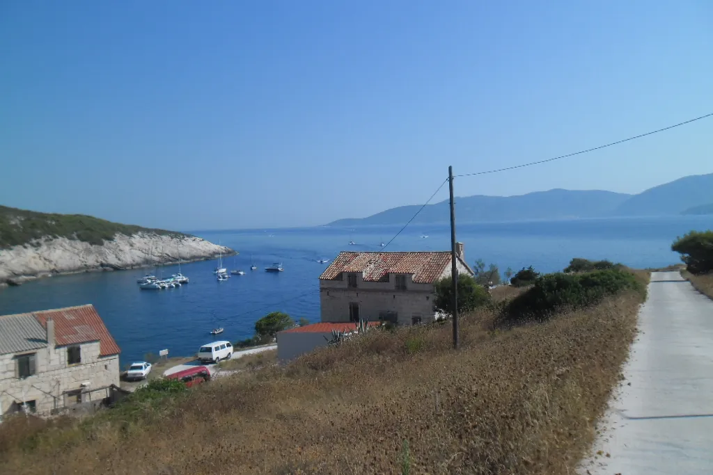 Mezuporat bay on Biševo from the road above, small boats and yachts moored in the blue bay below old stone houses, with Vis across the channel