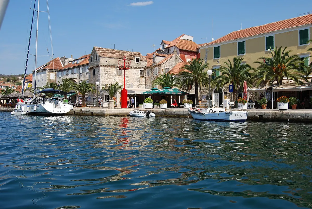 Milna waterfront seen from the water, stone houses, palms and yachts moored on the quay