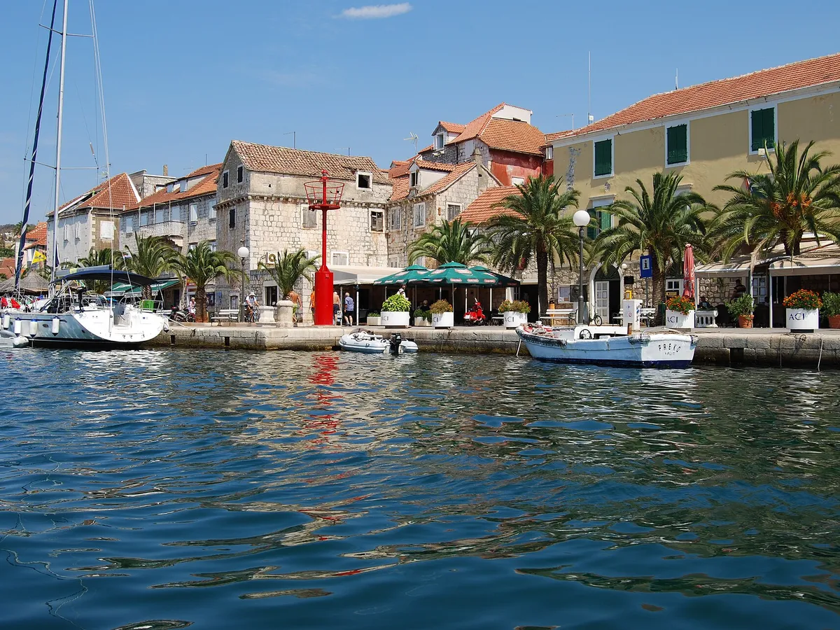 Milna waterfront seen from the water, stone houses, palms and yachts moored on the quay