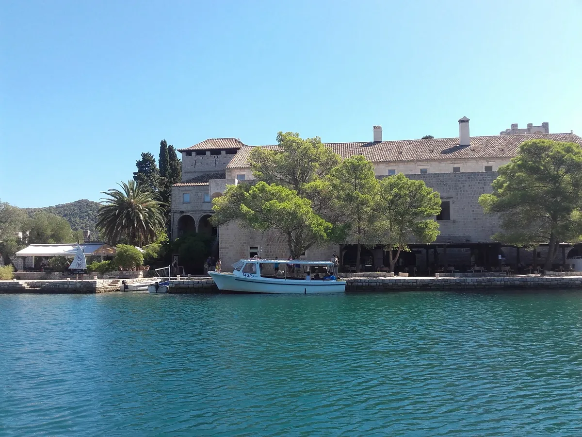 The Benedictine monastery on St Mary's islet in the Great Lake on Mljet, seen from the water, with the park's boat at the quay under the pines