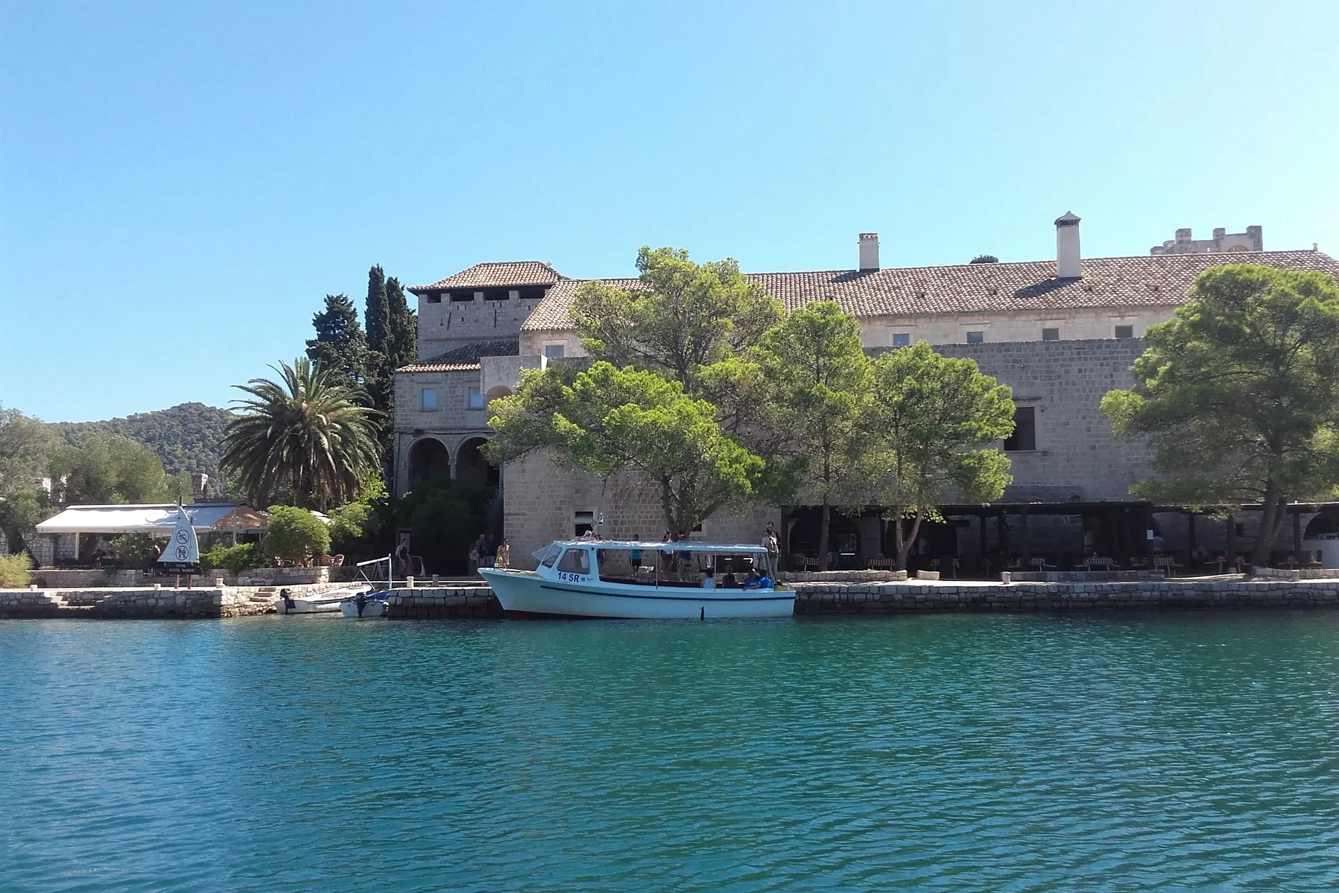 The Benedictine monastery on St Mary's islet in the Great Lake on Mljet, seen from the water, with the park's boat at the quay under the pines