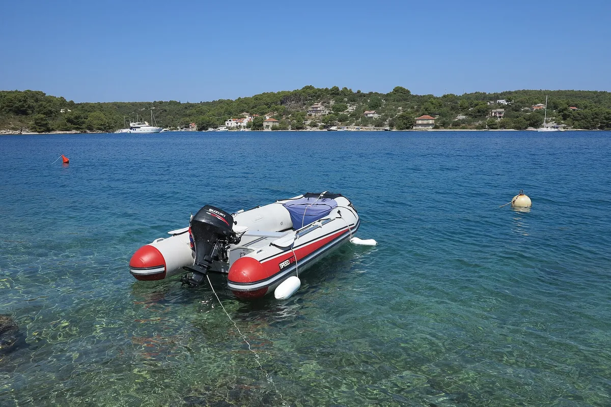 A tender on its mooring over clear water in Podkamenica cove, Nečujam bay, with a mooring buoy beside it and yachts moored along the far shore