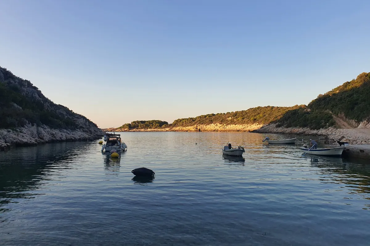 Oključna bay on Vis at dusk, small boats on their moorings in calm water between rocky wooded slopes, the evening sun on the far shore