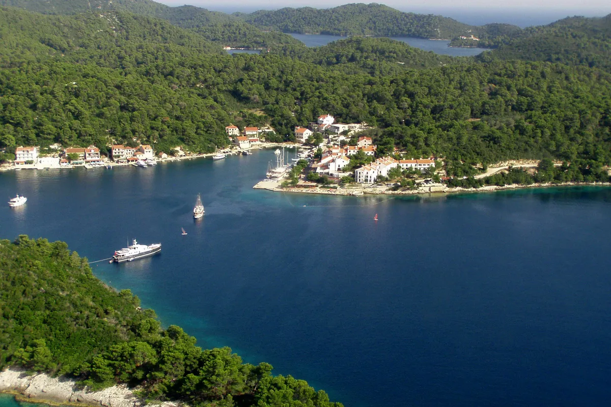 Pomena harbour on Mljet from above, with the village and its quay on the point, a gulet and a motor yacht at anchor and pine forest all around
