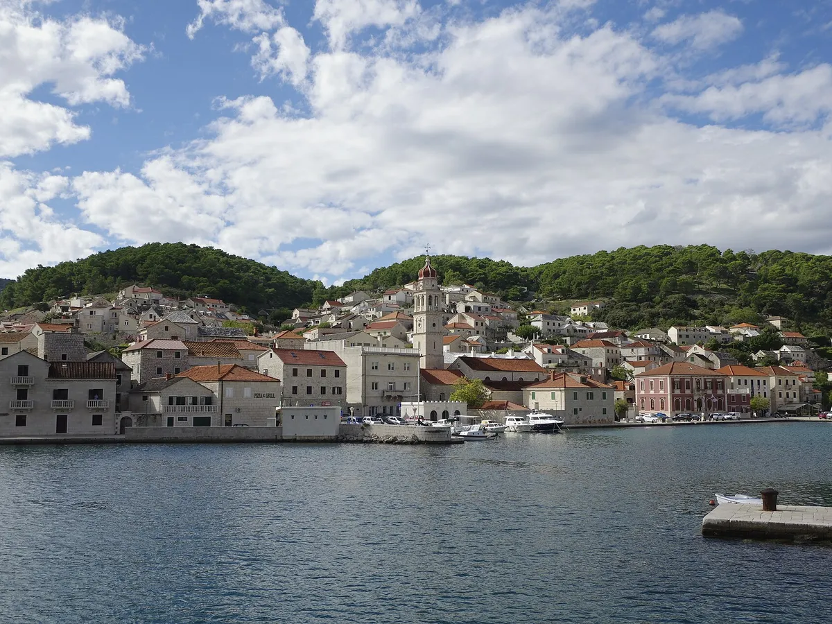 Pučišća harbour on Brač, a deep bay lined with white stone houses and the church bell tower, with small boats on the quay.