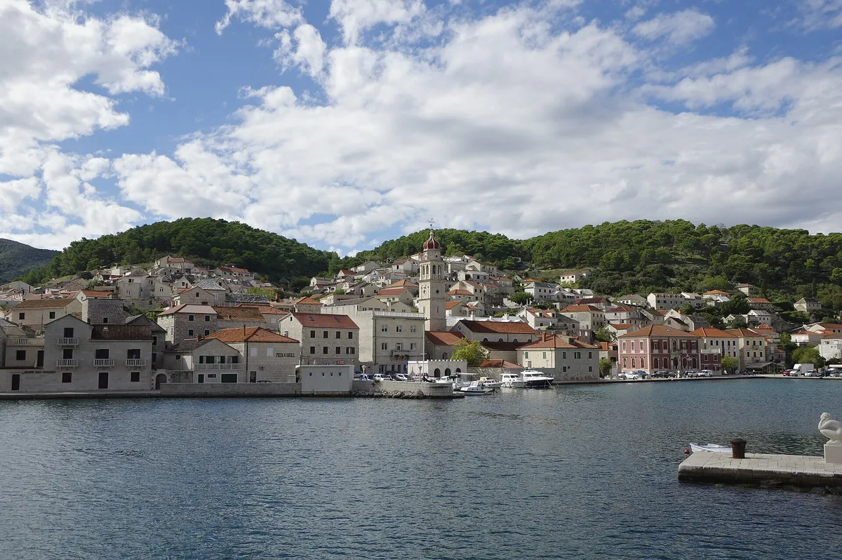 Pučišća harbour on Brač, a deep bay lined with white stone houses and the church bell tower, with small boats on the quay.
