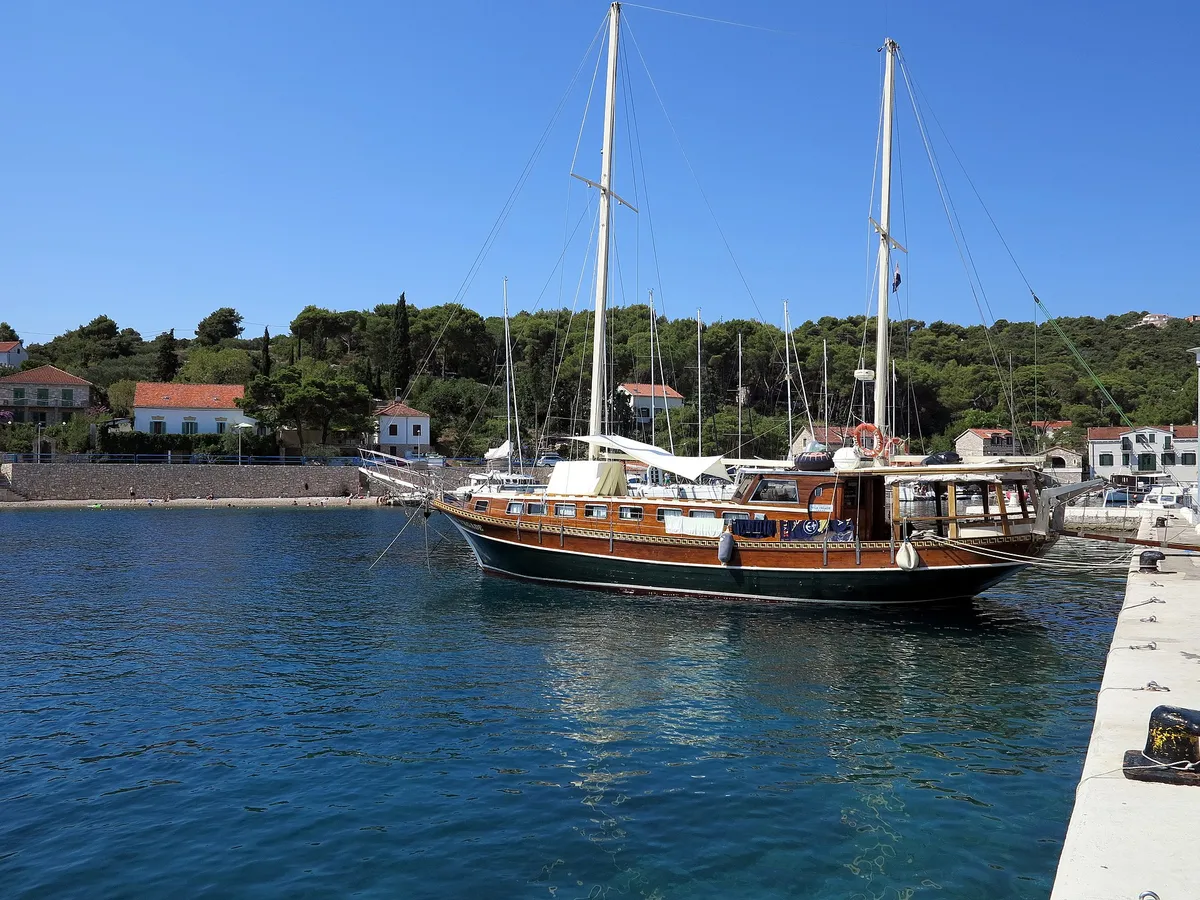 A gulet and yachts moored in Rogač bay on Šolta, next to the ferry quay, with pine woods and houses behind.