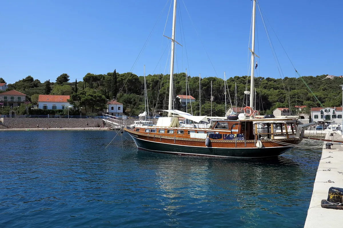 A gulet and yachts moored in Rogač bay on Šolta, next to the ferry quay, with pine woods and houses behind.