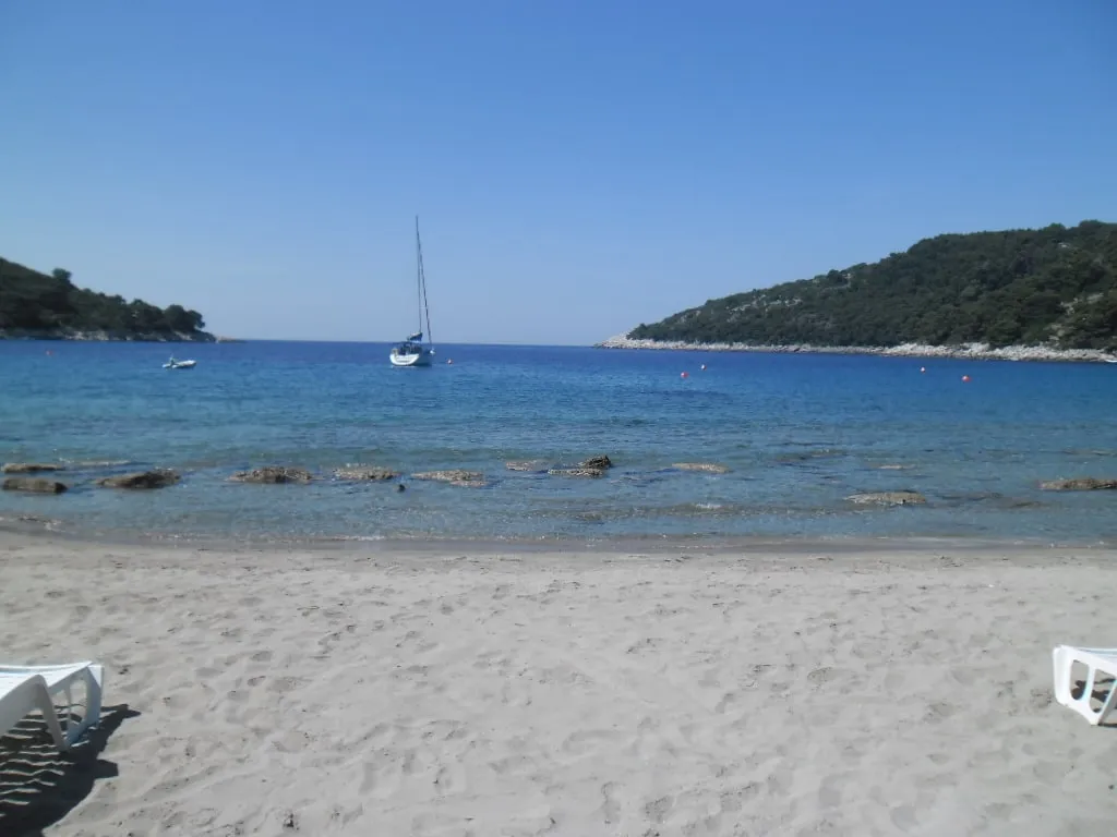The sandy beach at Saplunara on Mljet, with a yacht at anchor in the clear bay between two wooded headlands
