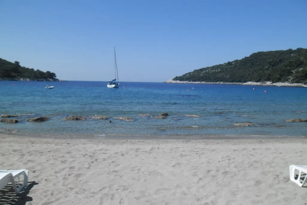 The sandy beach at Saplunara on Mljet, with a yacht at anchor in the clear bay between two wooded headlands