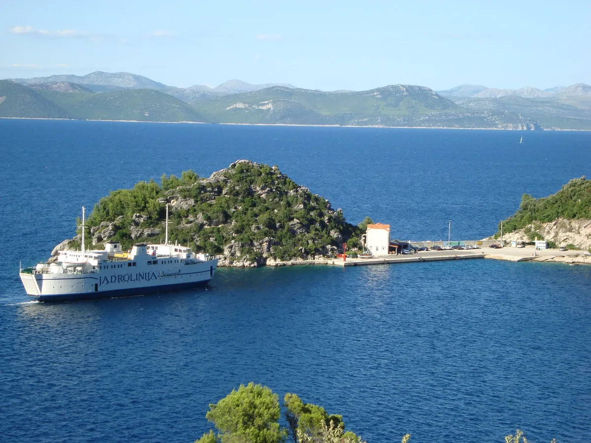 A Jadrolinija ferry arriving at the ferry port in Zaglavac bay by Sobra on Mljet, below a wooded islet, with Pelješac across the channel