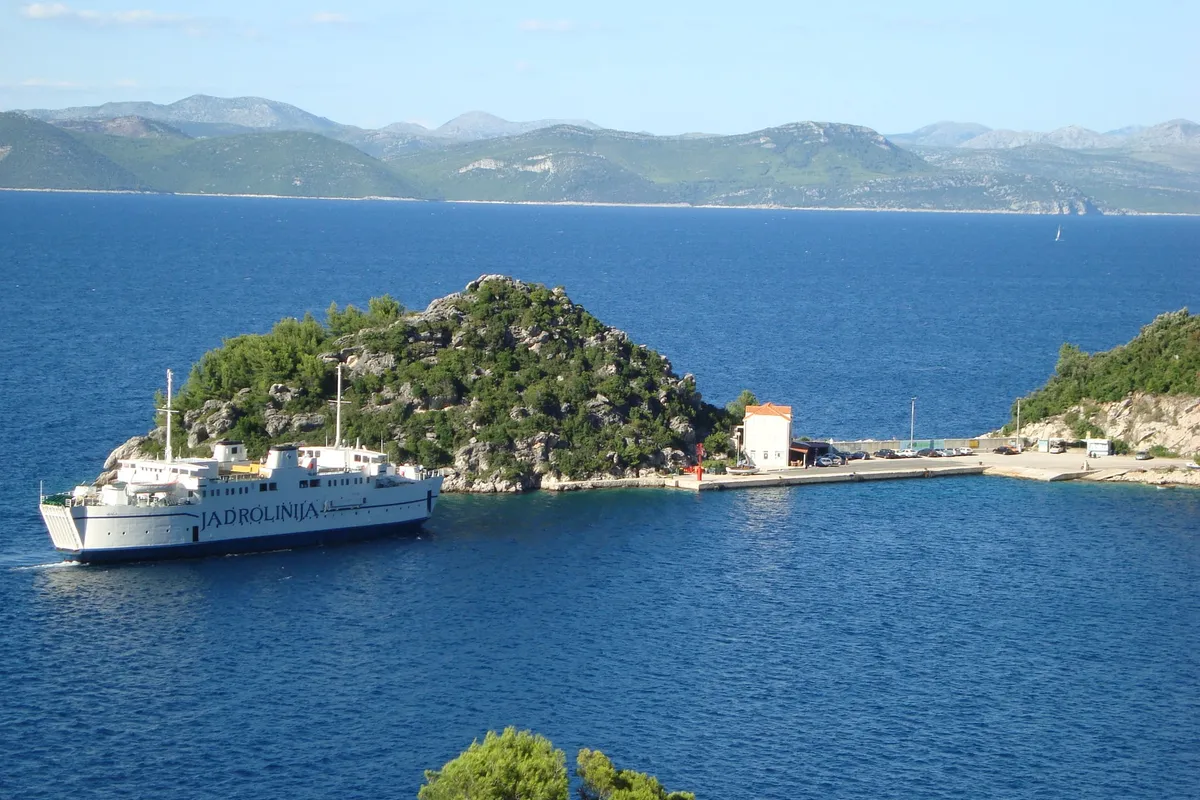 A Jadrolinija ferry arriving at the ferry port in Zaglavac bay by Sobra on Mljet, below a wooded islet, with Pelješac across the channel