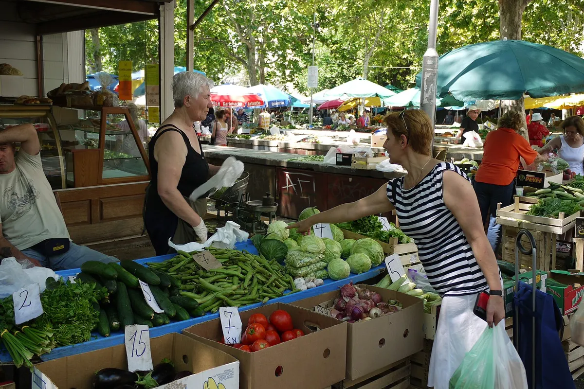 Vegetable stalls at Pazar, the green market in Split, with shoppers buying beans, cucumbers, cabbage and tomatoes under the trees