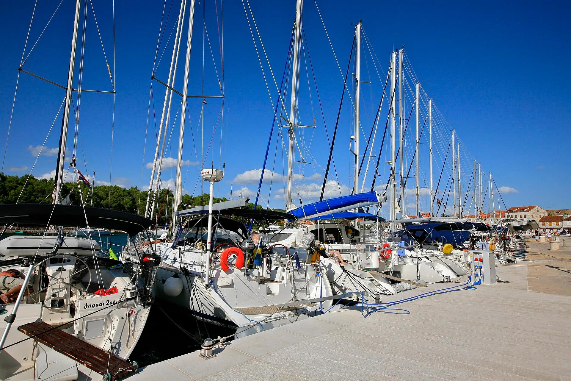 Visiting yachts moored stern-to along the town quay in Stari Grad, their passerelles down onto the stone quay, with the water and power posts along its edge