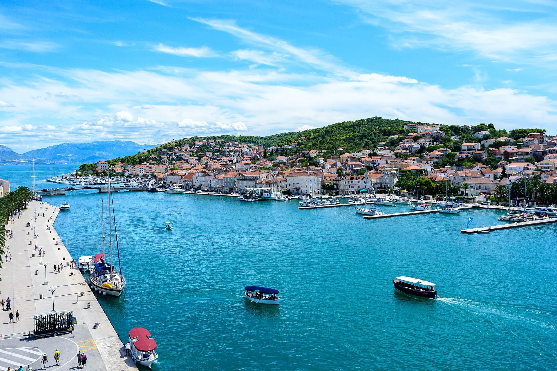 The Trogir channel from the Kamerlengo fortress, with a yacht on the Riva quay, water taxis crossing and the marina pontoons on the Čiovo shore where ACI Marina Trogir lies.