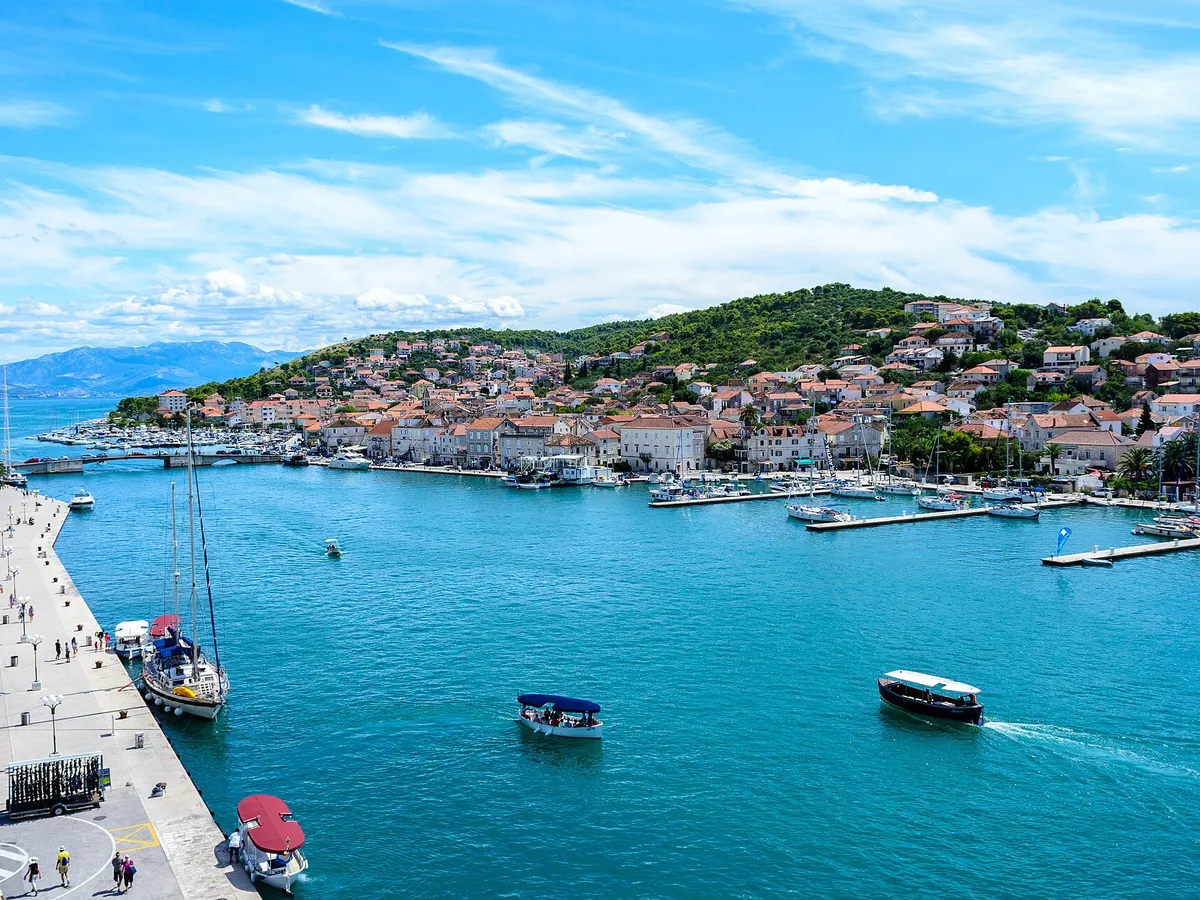 The Trogir channel from the Kamerlengo fortress, with a yacht on the Riva quay, water taxis crossing and the marina pontoons on the Čiovo shore where ACI Marina Trogir lies.