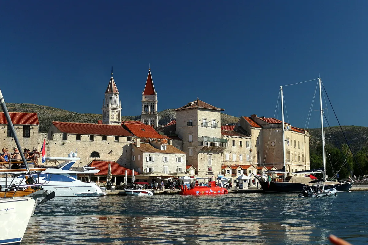 Trogir old town seen from a boat in the channel, with the cathedral and church towers, yachts and a gulet along the Riva.